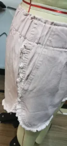 Detail of pink denim shorts with raw edge fringe and elastic waist on mannequin