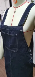 Close-up detail of dark blue denim pinafore dress with front pocket and side buttons