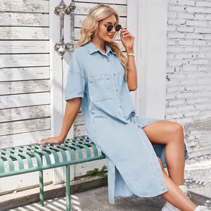 Side view of a woman wearing a loose light blue denim short sleeve shirt dress with side slits.