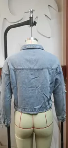 Detailed back view of a light blue distressed denim jacket shown on a dress form