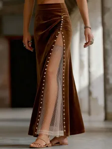 Détail d'une jupe longue en velours marron avec fente haute, tulle et perles élégantes.