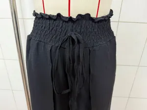 Close-up of black wide-leg trousers featuring a smocked high waist with drawstring detail.