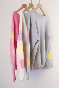 Loose boat neck knit sweaters with floral sleeve patterns displayed on wooden hangers