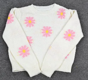 Detailed view of soft white knit sweater with vibrant pink and yellow daisy patterns.