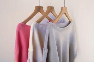 Close-up detail of oversized boat neck knit sweaters in pink, white, and grey colors
