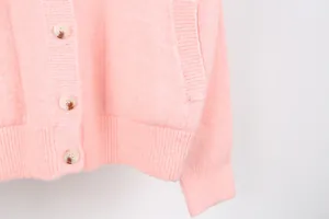 Detailed macro shot of a soft pink knitted cardigan with amber buttons and pocket