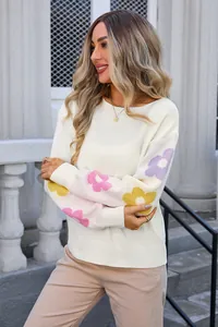 Detail of white loose knit sweater featuring colorful flower patterns on the sleeves.