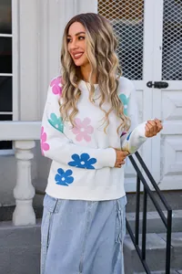 Detailed view of floral print round neck white knit sweater worn by model in outdoor setting