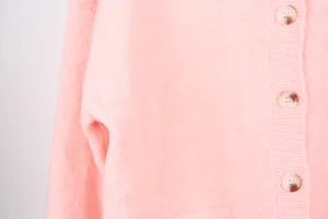 Detailed close-up of a soft pink knitted cardigan showing buttons and pocket texture