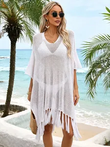 Woman wears a white crochet beach cover-up with tassels on a sunny tropical beach