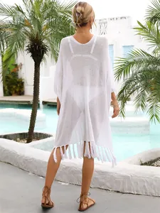 Back view of a white loose-knit crochet beach cover-up with tassel trim by a tropical pool