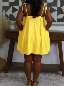 Back view of a yellow loose babydoll summer dress with tie straps and button details.