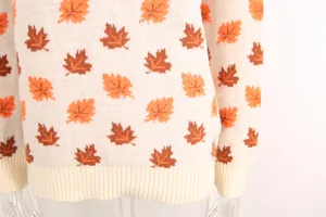 Close-up of knit sweater featuring orange and brown maple leaf patterns with ribbed hem