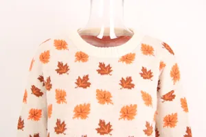 Close-up of the crew neck and maple leaf pattern on a cream-colored knit sweater.
