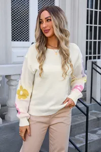Detail view of white loose knit sweater featuring colorful floral patterns on sleeves.