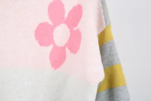 Close-up detail of a knitted sweater with a pink flower pattern and striped sleeve