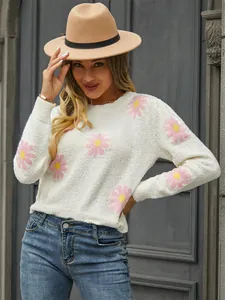 Detail view of a white knit sweater with pink daisy floral patterns worn by a model.