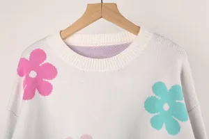 Close-up of white knit sweater featuring colorful floral patterns and ribbed crew neck.