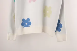 Macro detail view of white knit sweater hem and cuffs with colorful floral patterns.