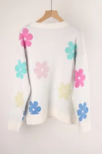Detail of white knitted sweater featuring vibrant multi-colored flower patterns and ribbed hem.