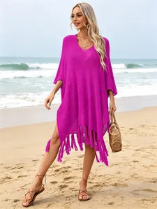 Model wearing a stylish magenta oversized knit beach cover-up with fringe tassels on the sand.