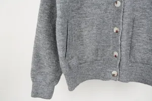 Macro view showing the soft knit texture and tortoise buttons of a grey wool cardigan.