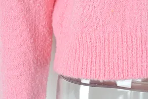Close-up of pink bouclé knit fabric texture and ribbed hem detail on a fashion sweater