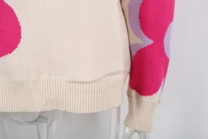 Close-up detail of cream knitted sweater featuring large pink floral print and ribbed hem