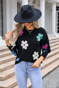 Close-up of black knitted sweater featuring colorful flower patterns and round neck.