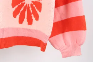 Close-up of pink and red knitted sweater with flower pattern and striped sleeve