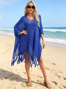 Detail of vibrant blue crochet poncho cover-up with playful tassels on a sunny beach