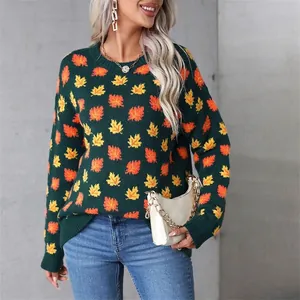 Detailed view of dark green knit sweater featuring vibrant orange and yellow maple leaf patterns.