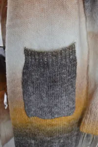 Detailed view of soft rainbow tie-dye knit cardigan texture with a contrast grey pocket.