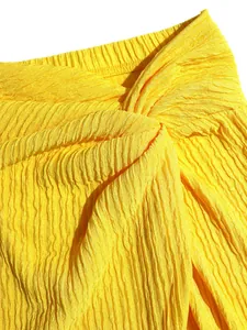 Detail view of the twisted knot and pleated texture on a yellow summer holiday skirt set.
