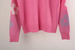 Detailed macro view of pink knitted sweater featuring floral sleeve patterns and ribbed cuffs.