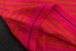 Macrodetail van roze en oranje gestreepte gebreide stof met decoratieve metalen stiksels erop.