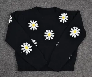 Close-up detail of a soft black knitted sweater featuring vibrant white daisy floral patterns