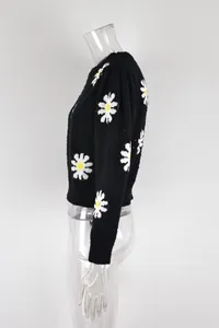 Side profile detail of black round neck sweater with white daisy floral knit patterns.