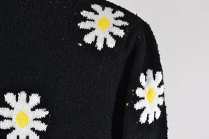 Close-up detail of white daisy floral pattern on a black knit crewneck sweater.