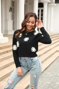 Full-body view of a model in a black daisy knit sweater with light blue ripped jeans.