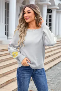 Detail of a grey boat neck knit sweater with floral sleeve patterns on a model outdoors.