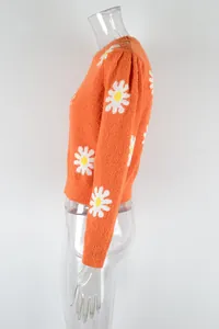 Side view of a bright orange knit sweater featuring white daisy floral patterns on sleeves
