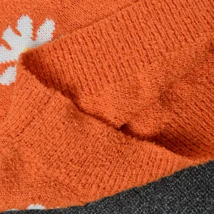 Detailed macro view of soft orange knitted fabric featuring a white daisy flower pattern