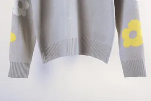 Detailed view of a grey knitted sweater with yellow floral patterns on sleeves and ribbed hem
