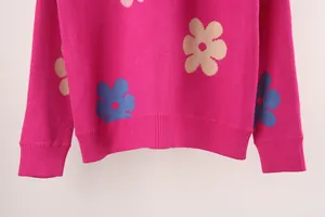 Close-up detail of a pink knitted sweater with colorful floral patterns and ribbed hem.