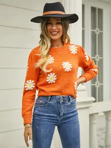 Detailed view of women's orange knitted sweater with white daisy patterns and round neckline