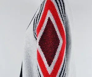 Macro view of the red and black diamond knit pattern on a white cardigan sleeve.