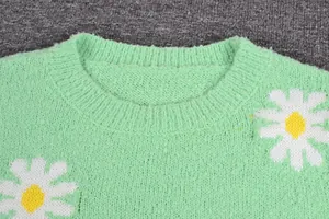 Macro detail view showing the crew neckline of a green knitted sweater with daisy pattern