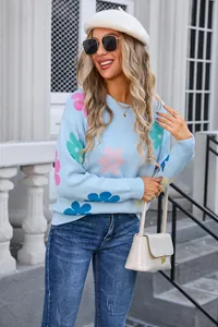Detail view of light blue round neck sweater featuring colorful flower patterns on model.