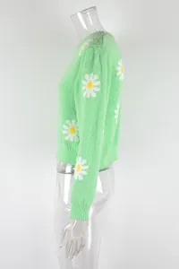 Side view of a green knit sweater with white daisy floral patterns on a mannequin.